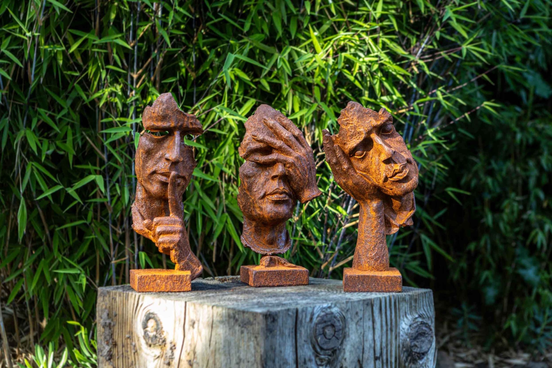 Drie roestige tuinbeelden in een bamboebos