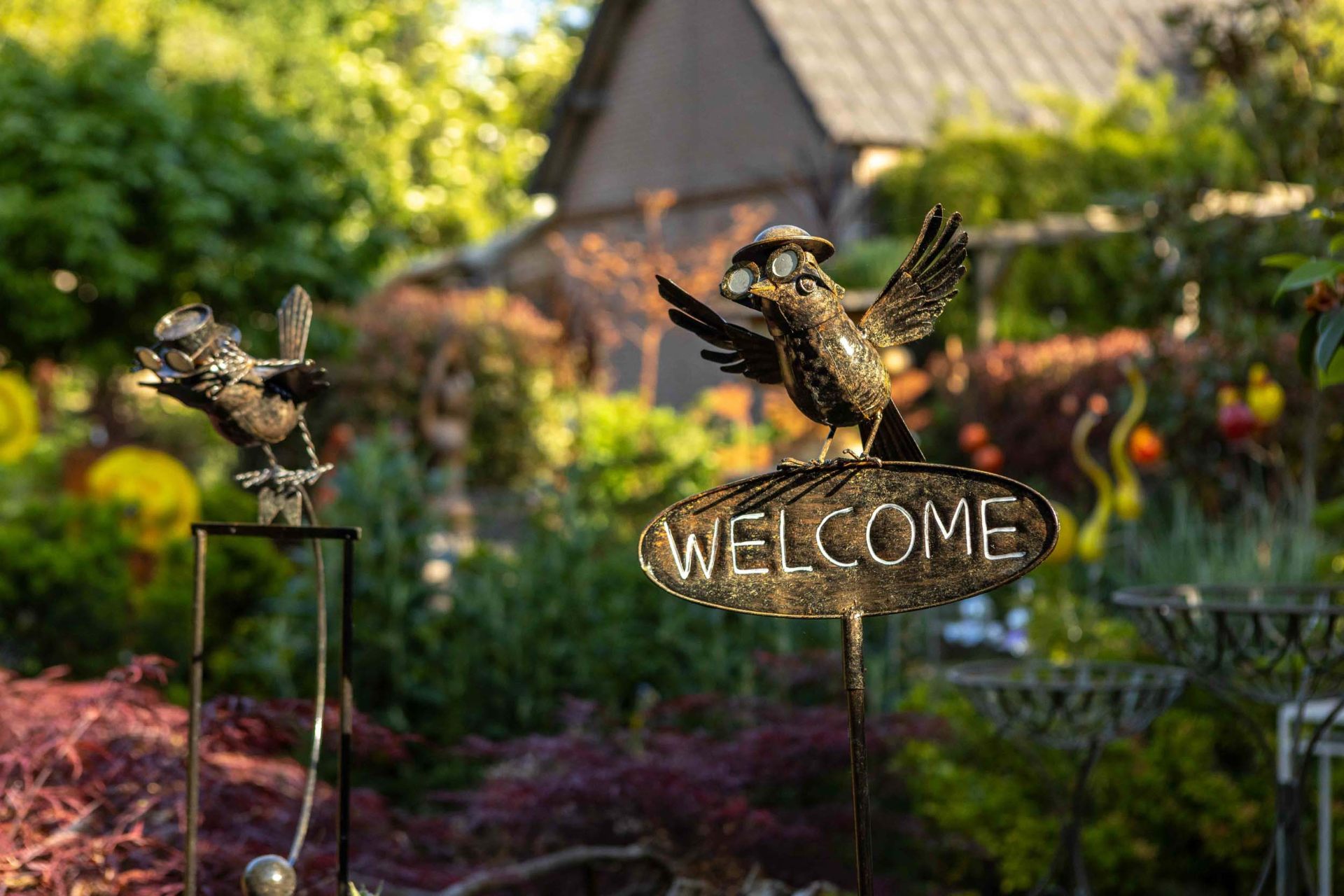 Metalen vogelfiguren met welkomstbord in de tuin