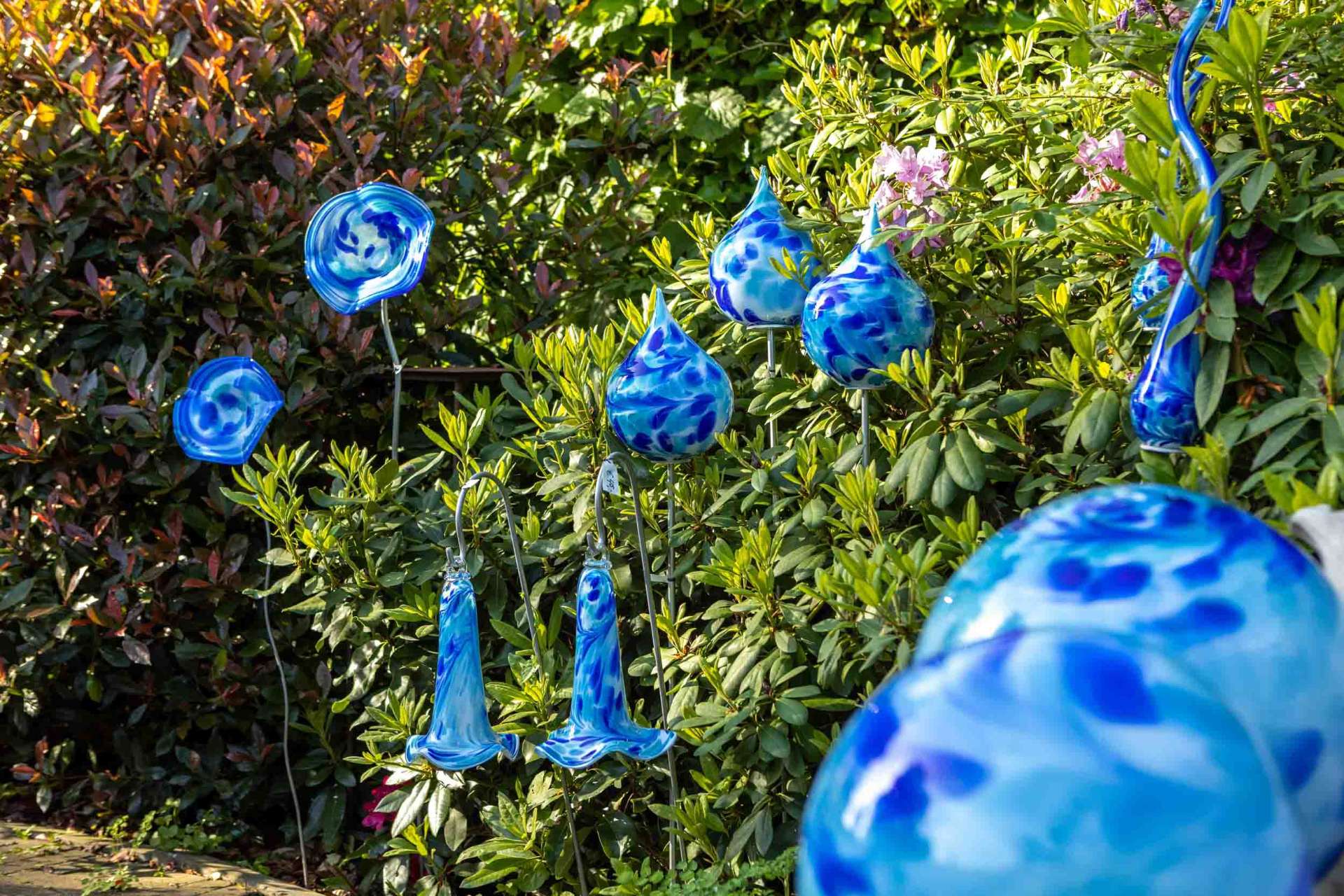 Blauwe glaskunst druppels en bloemen tussen de rododendrons